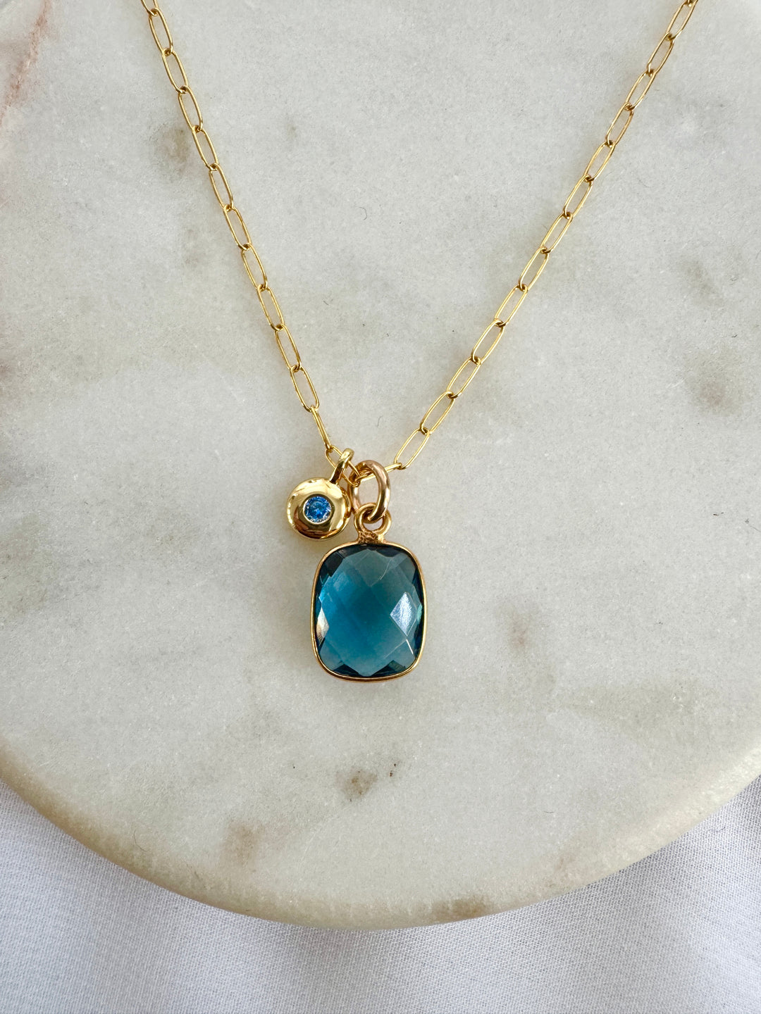 Gold necklace with a blue iolite rectangle pendant with a round small charm