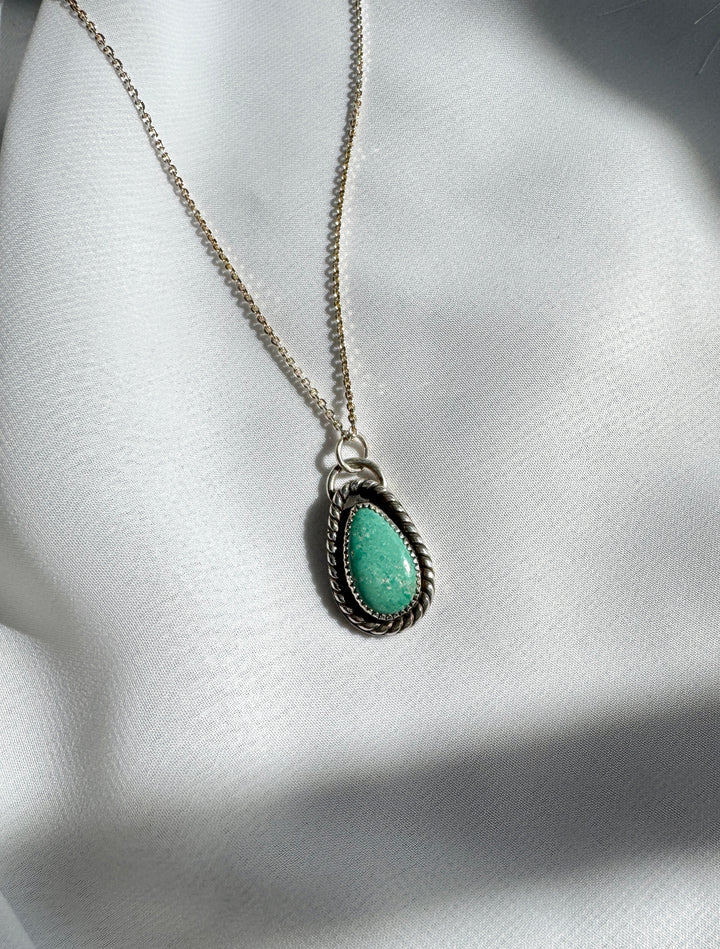 A sterling silver necklace with a teardrop-shaped turquoise pendant, displayed against a white fabric background.